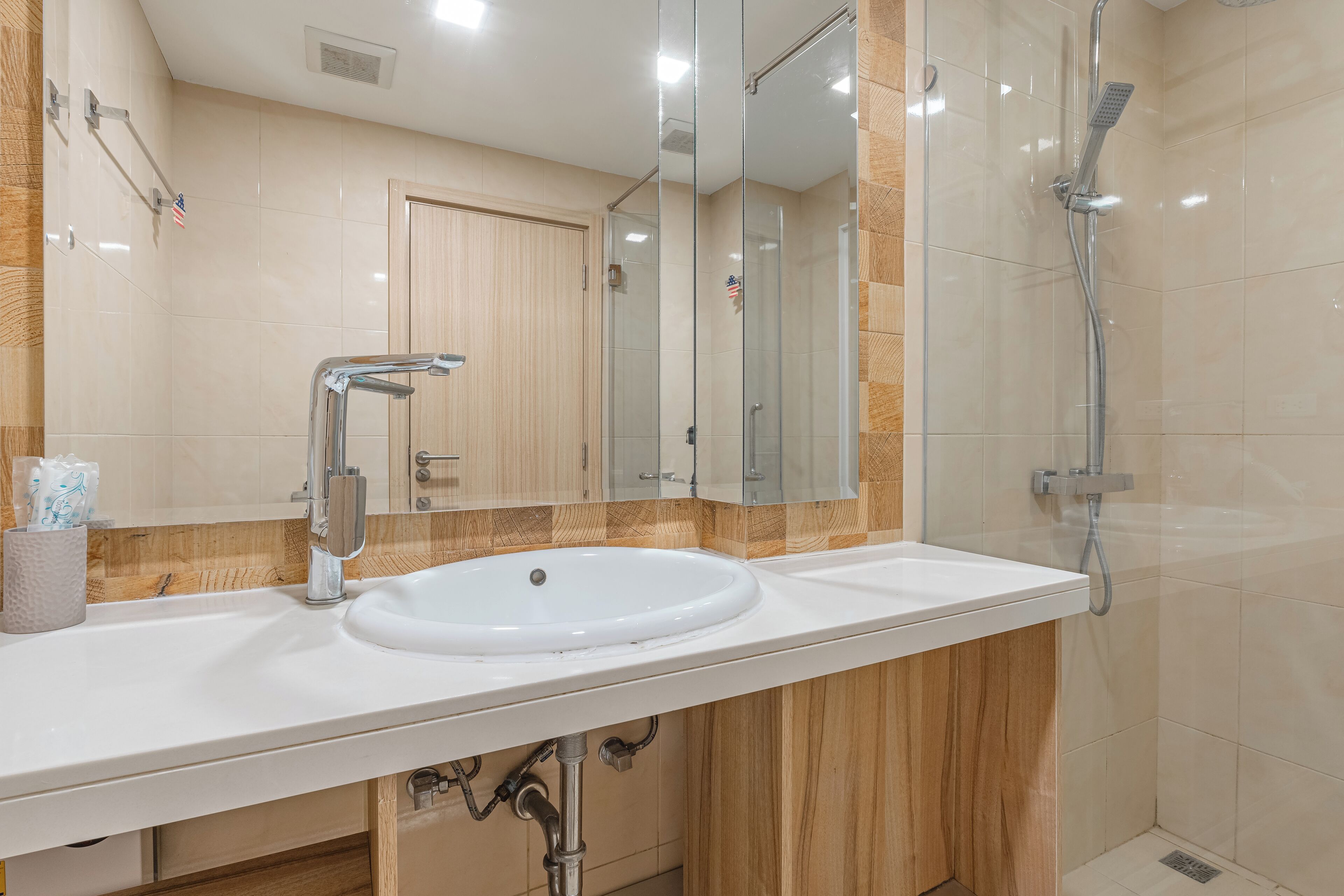 Un baño moderno con un lavamanos blanco, un espejo grande y una ducha con mampara de vidrio.