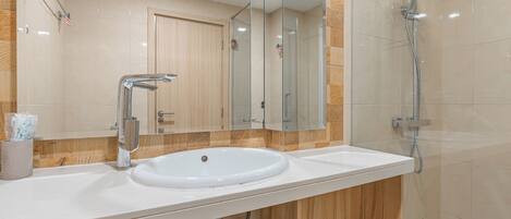 Un baño moderno con un lavamanos blanco, un espejo grande y una ducha con mampara de vidrio.