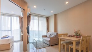 A modern living room with a sofa, a dining table with chairs, a glass coffee table, and a TV. - City Garden Tower by Pattaya Holiday (Pattaya)