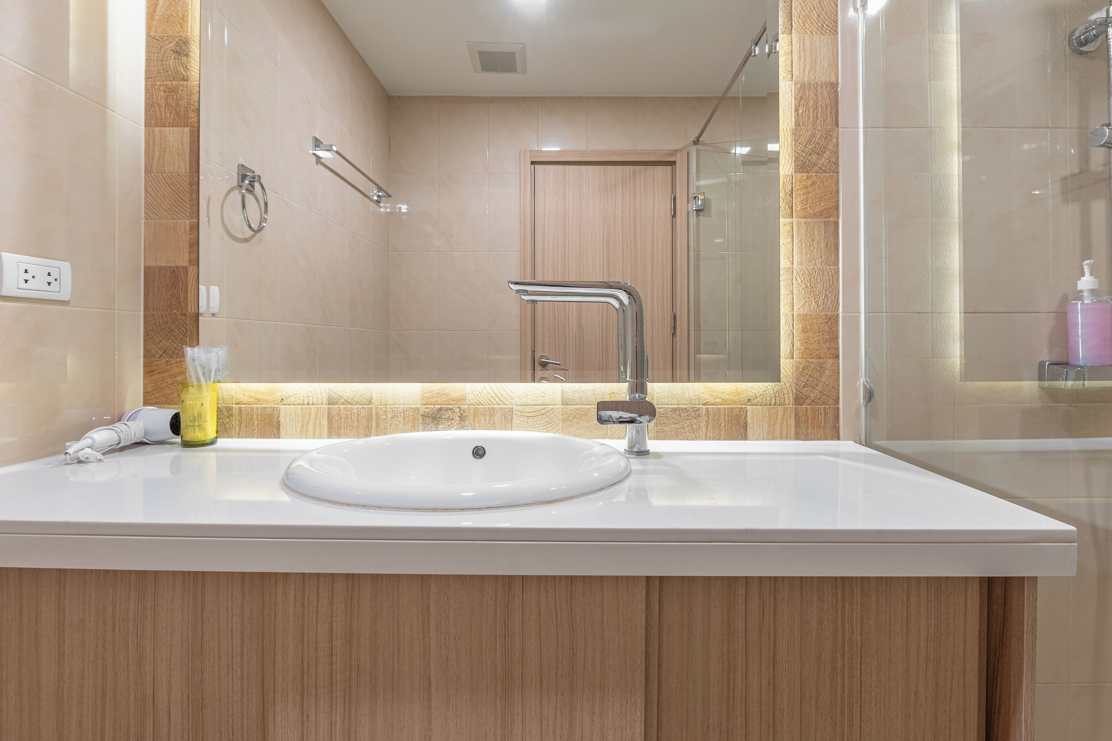A modern bathroom with a white sink, wooden vanity, and a glass shower enclosure.