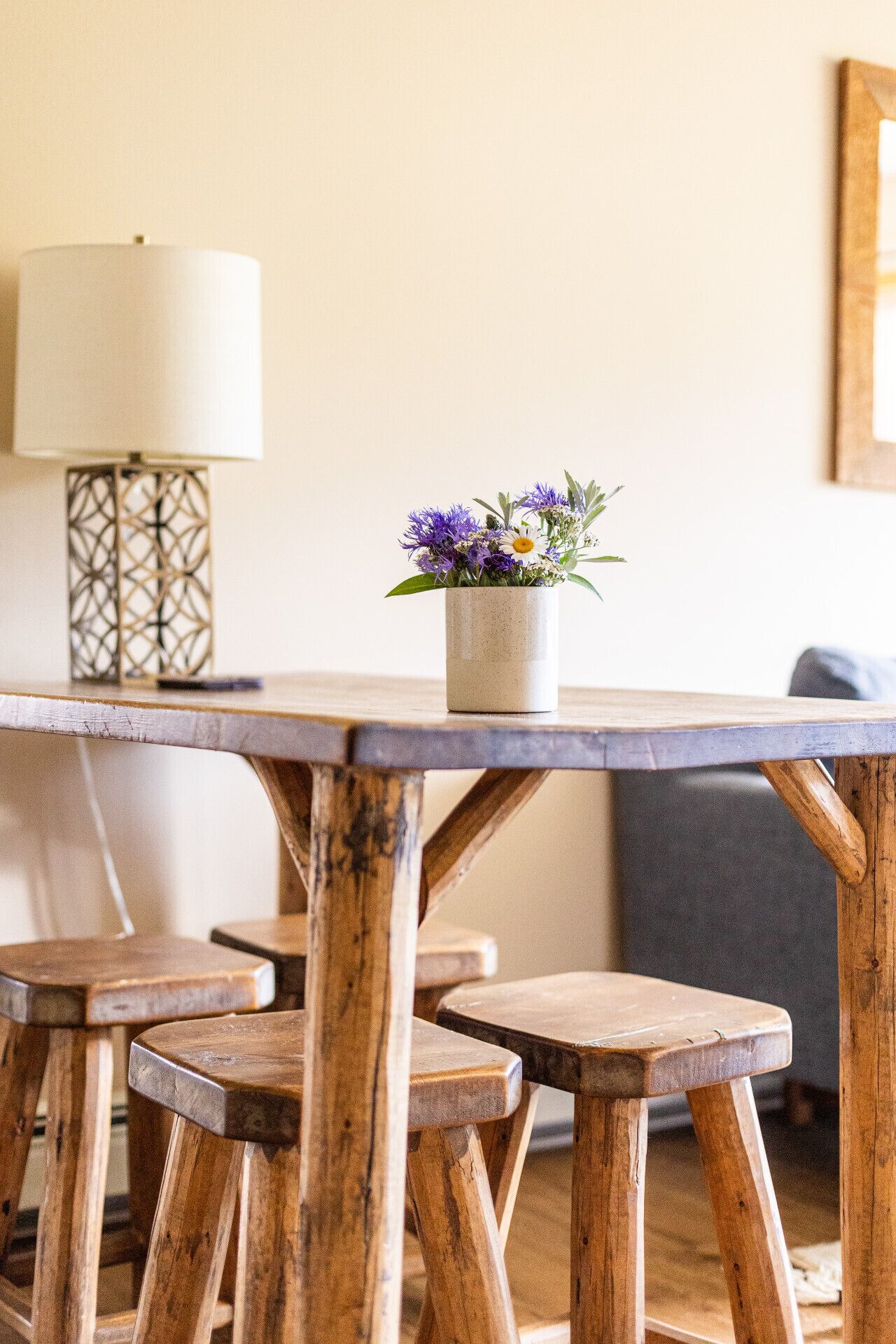 Una mesa de madera rústica con un florero, una lámpara y una silla en una habitación acogedora.