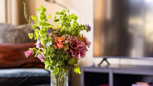 Une table basse ronde en bois sur laquelle repose un vase en verre transparent contenant un bouquet de fleurs.