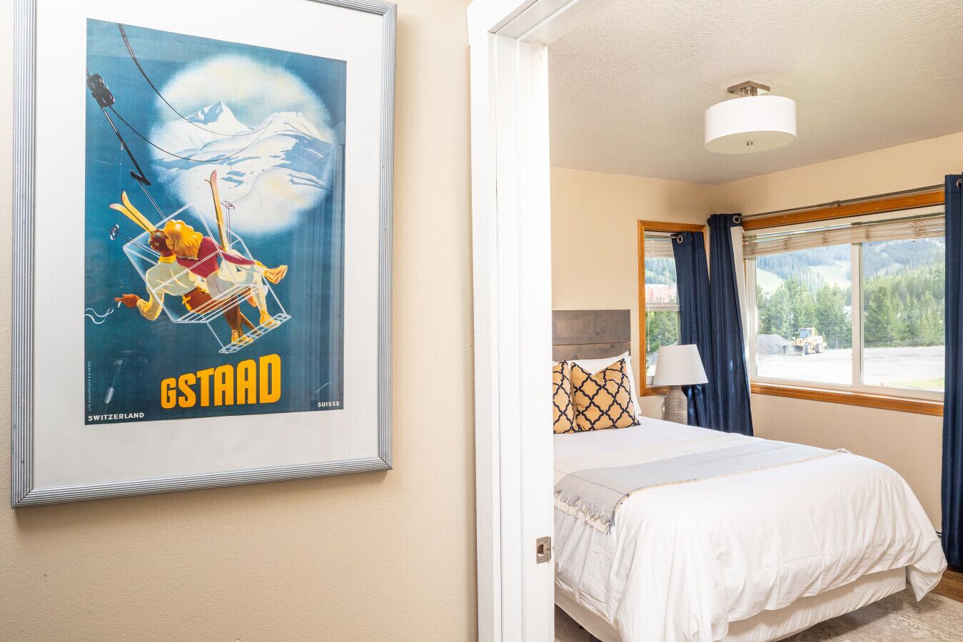 A hotel room with a bed, a window with curtains, a framed picture on the wall, and a lamp on the bedside table.
