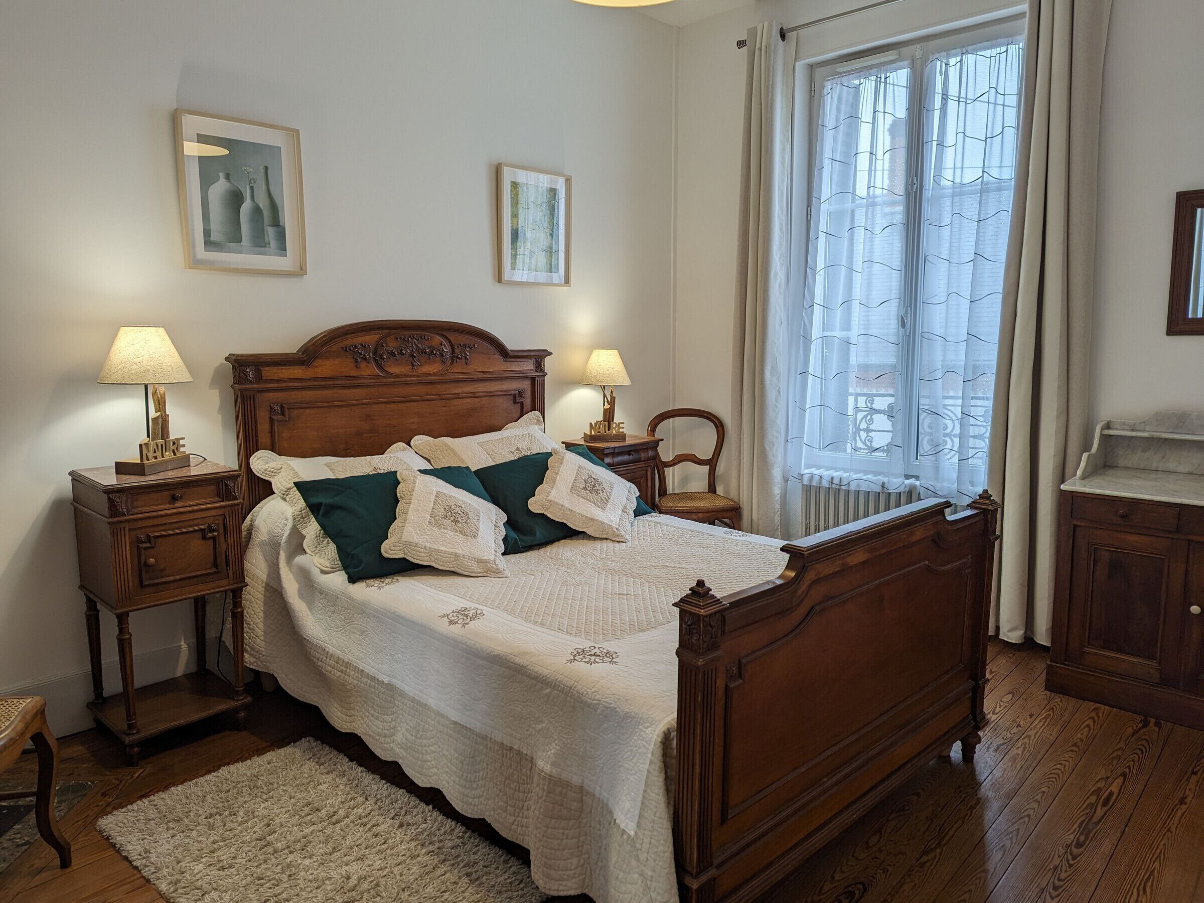 A neatly made bed with a wooden headboard, two bedside tables with lamps, and a window with curtains.