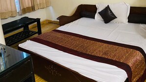 A hotel room with a large bed, a desk, and a window with curtains. - Hotel Ashoka International (New Delhi)