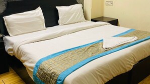 A bed with white linens, a dark headboard, and a blue and beige blanket. - Hotel Ashoka International (New Delhi)