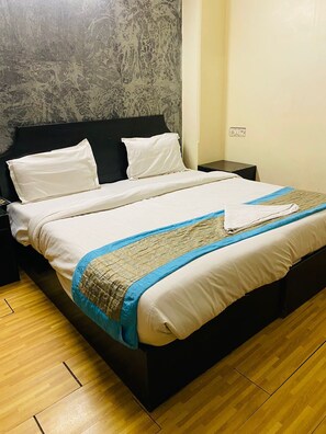 Un lit avec des draps blancs, une tête de lit sombre et une couverture bleue et beige.