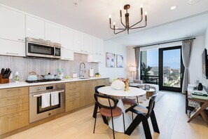 A modern kitchen with a built-in microwave, oven, and gas stove. There is a dining area with a round table and chairs, and a large window offering a city view.