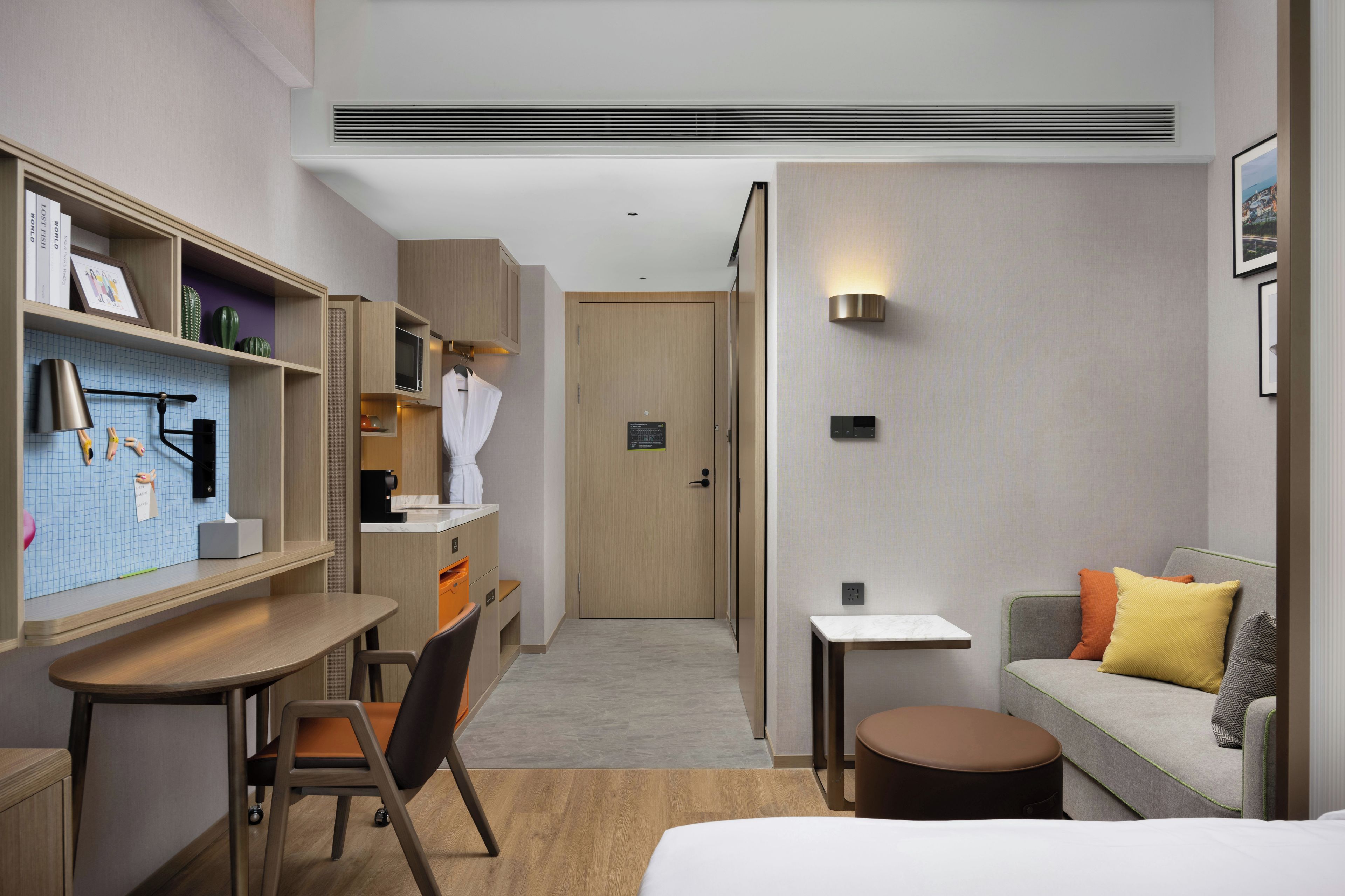 Habitación de hotel con escritorio, silla, sofá y una mesita de noche con lámpara.
