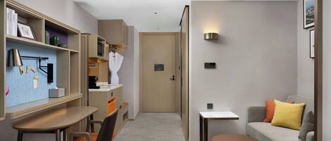 Habitación de hotel con escritorio, silla, sofá y una mesita de noche con lámpara.