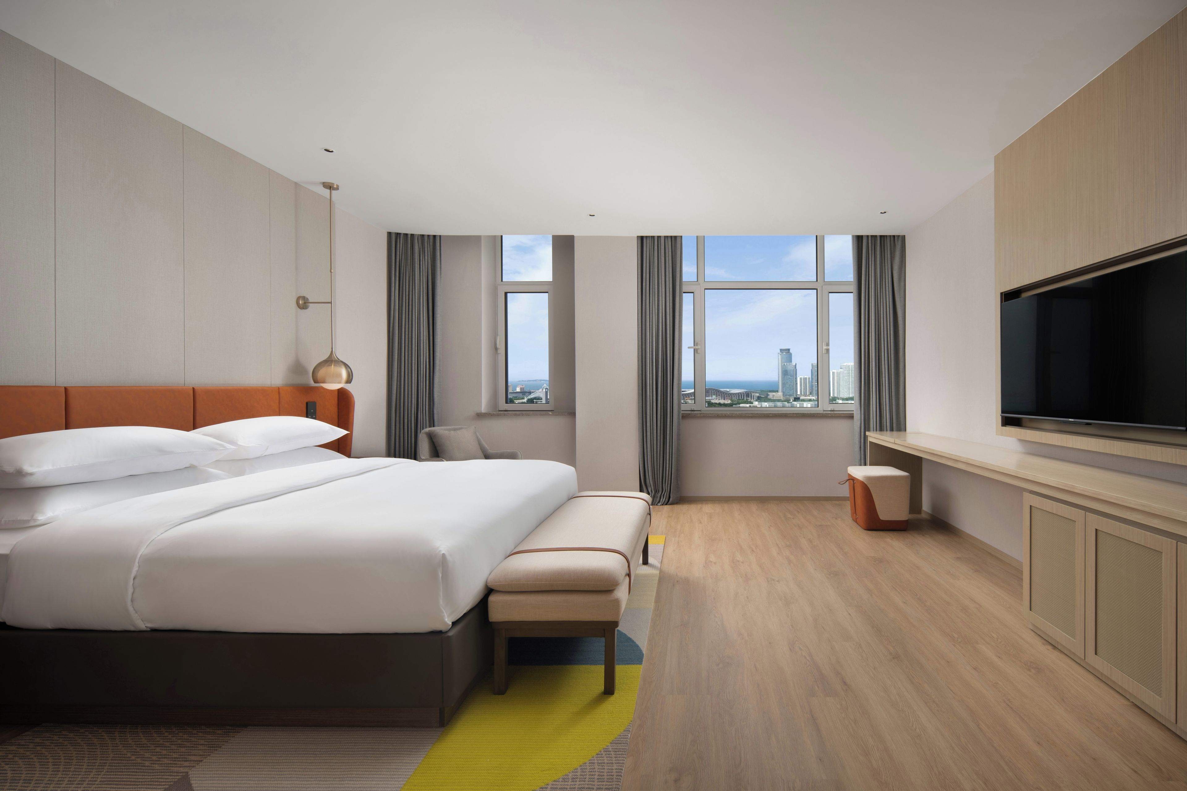 A hotel room with a large bed, a TV, a desk, and a view of the cityscape.