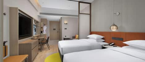 A hotel room with two beds, a desk, a television, and a bathroom.