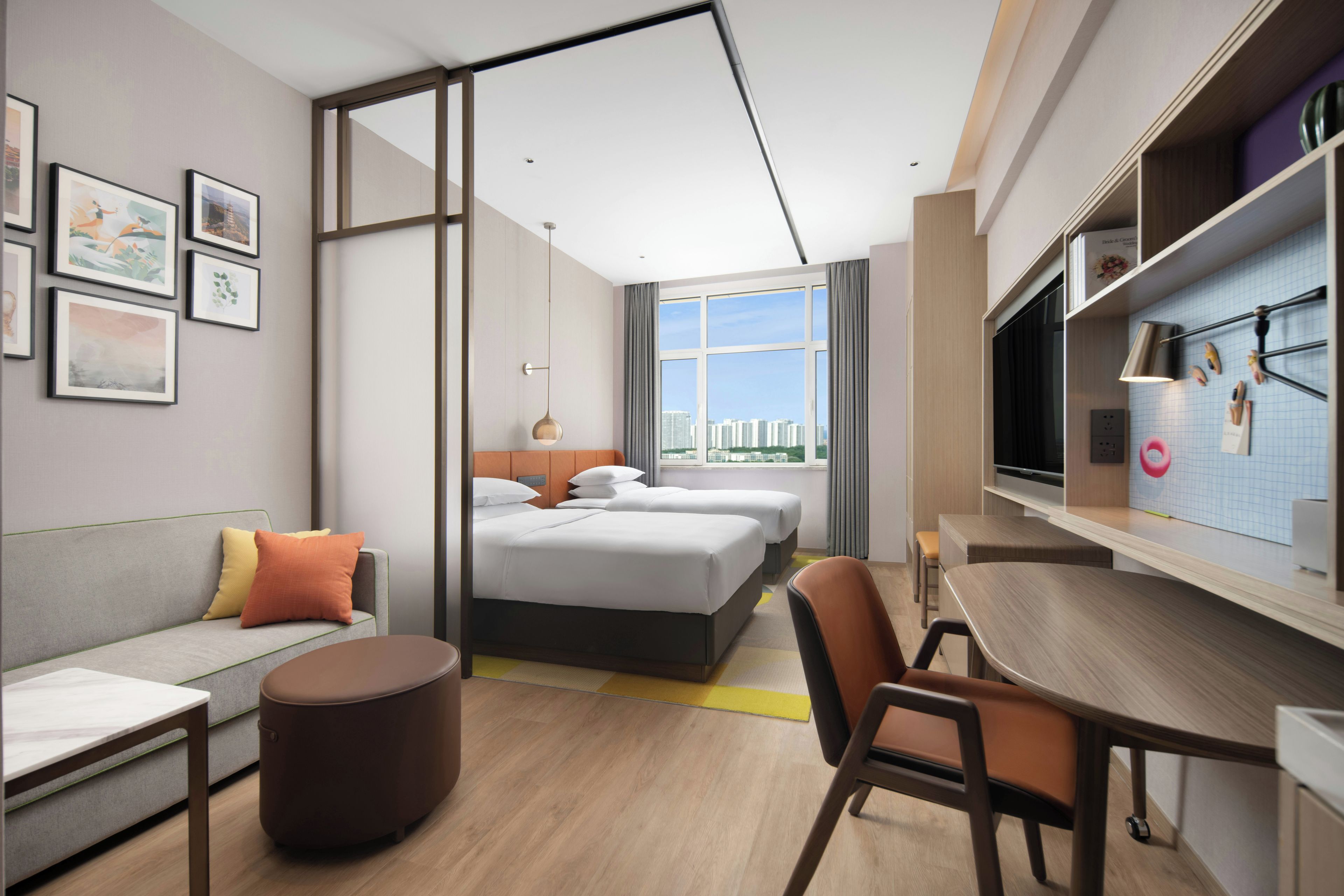 A modern hotel room with a large bed, a sofa, a dining table, and a view of the city.