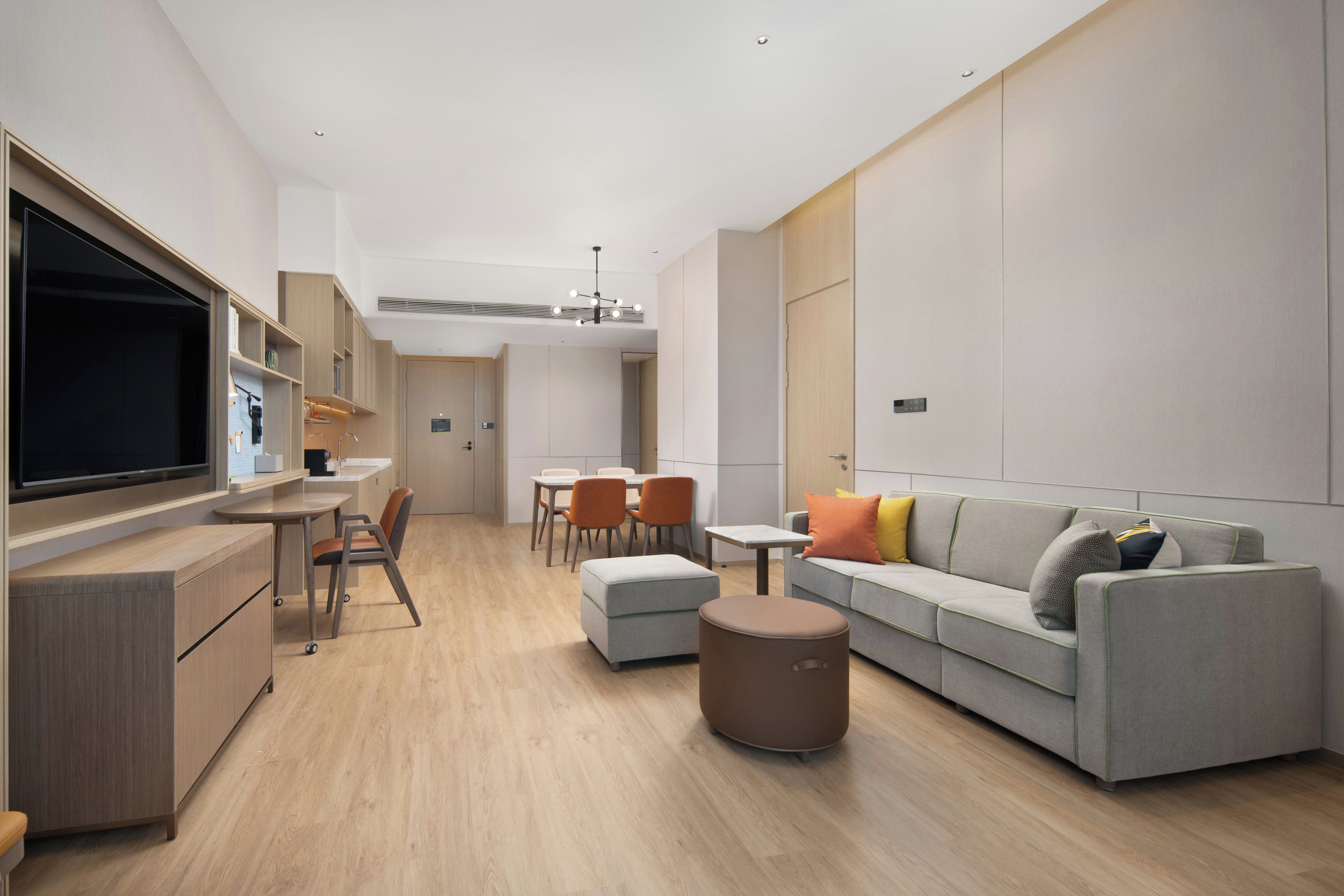 A modern living room with a sofa, ottoman, and a television. There is a dining area with chairs and a table.