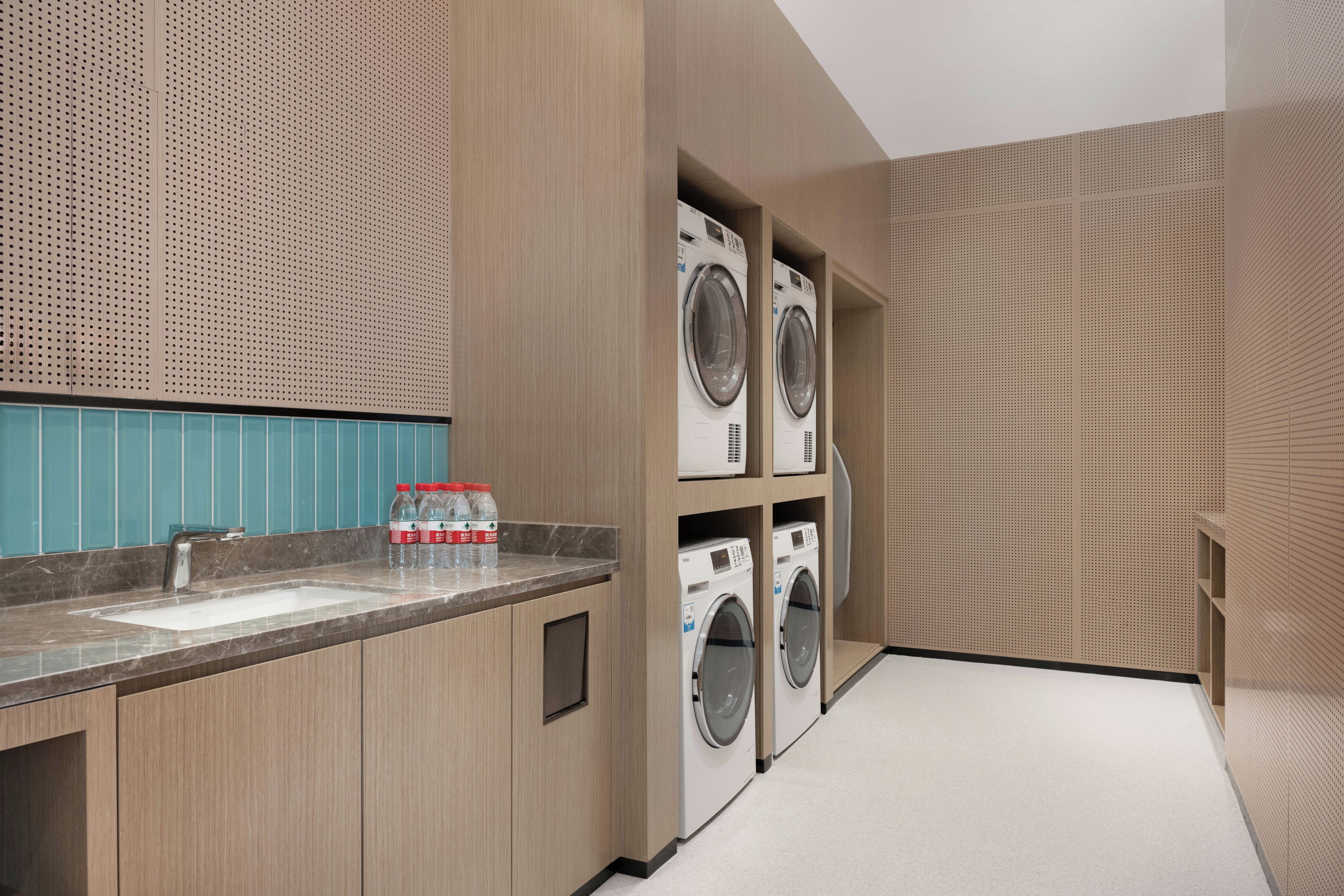 A modern laundry room with built-in washers and dryers, a marble countertop, and a blue tiled backsplash.