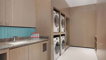 A modern laundry room with built-in washers and dryers, a marble countertop, and a blue tiled backsplash.