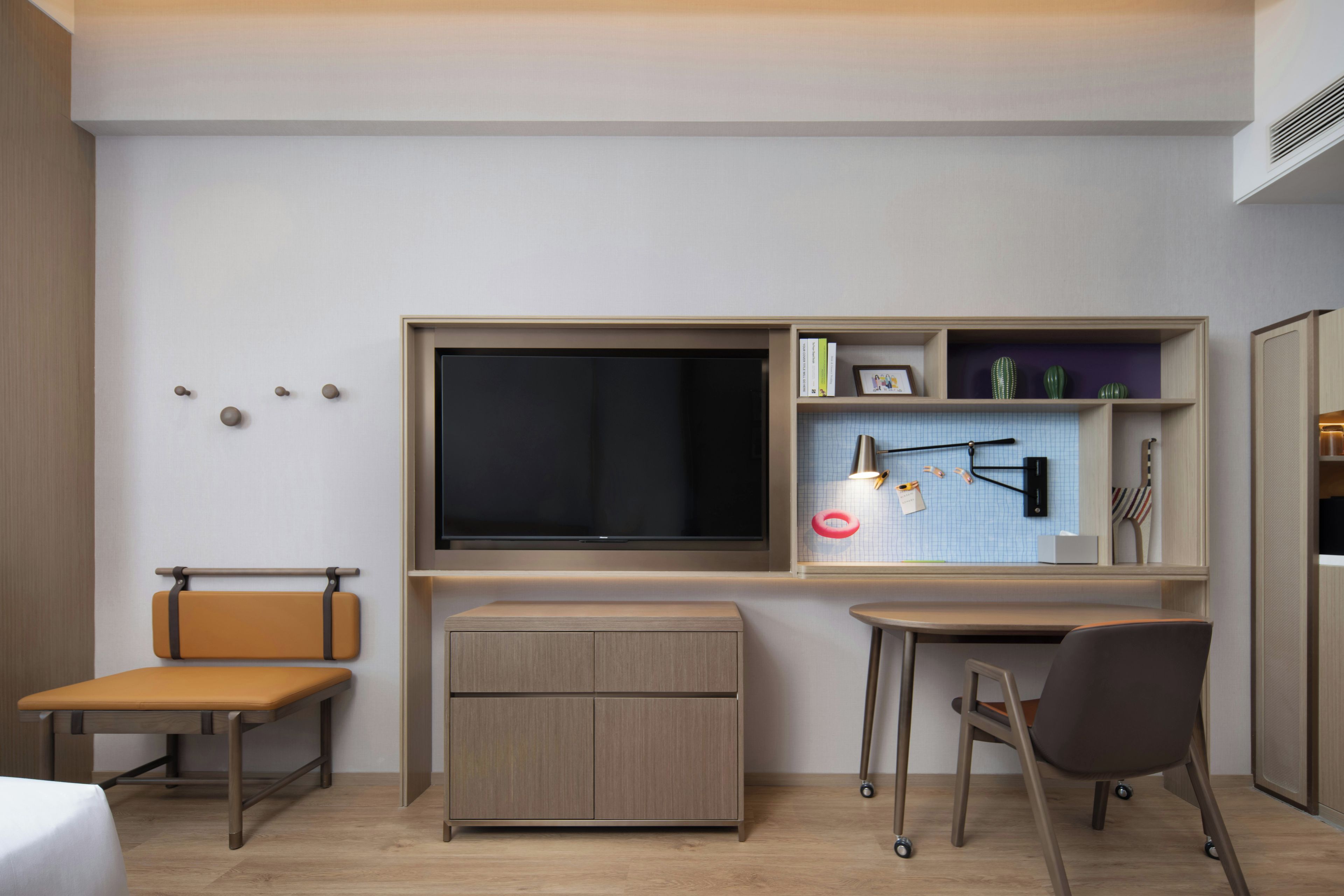 A modern room with a flat-screen TV, a desk, a chair, a bench, and a small cabinet.
