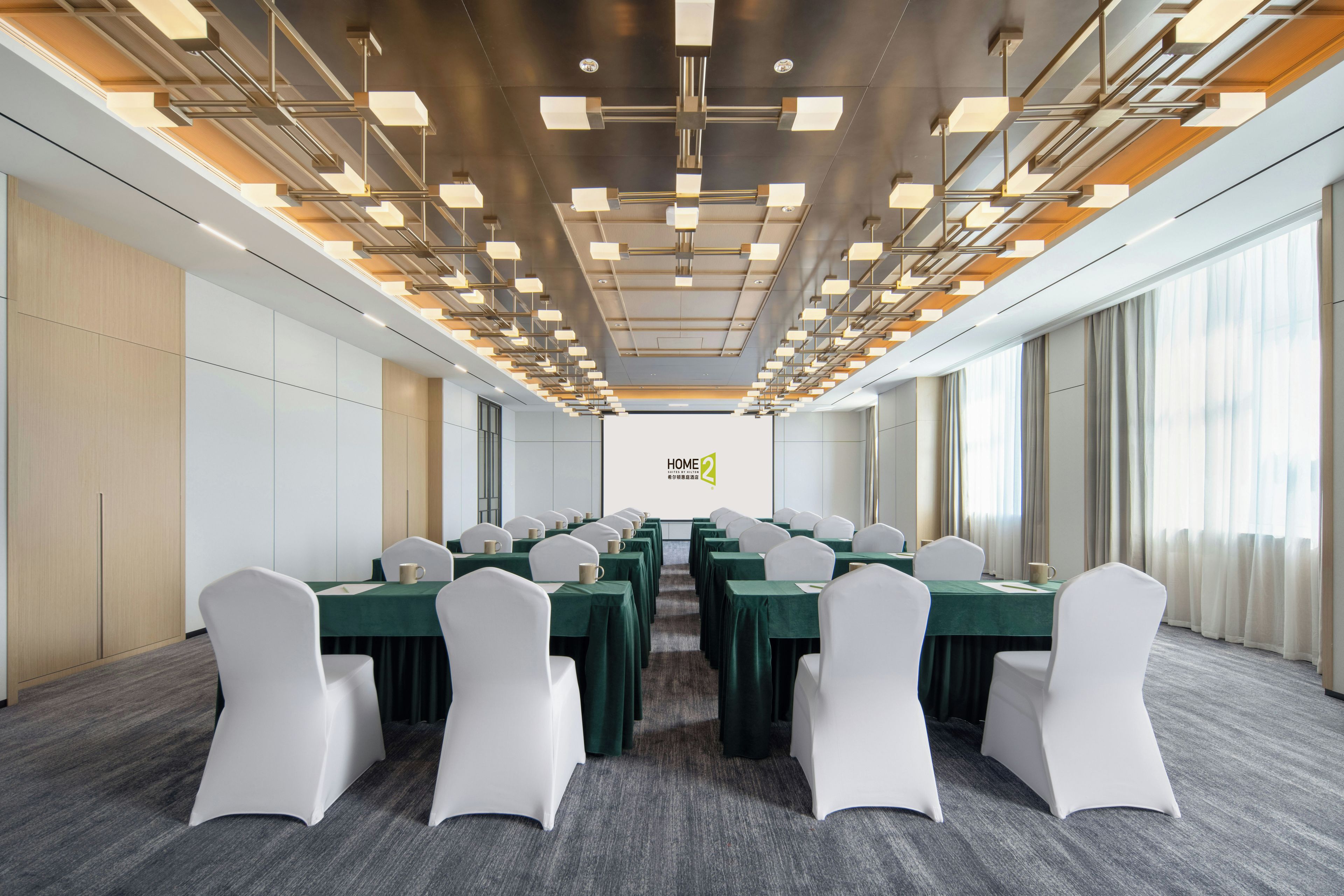 A conference room with a long table, white chairs, and a modern ceiling design.