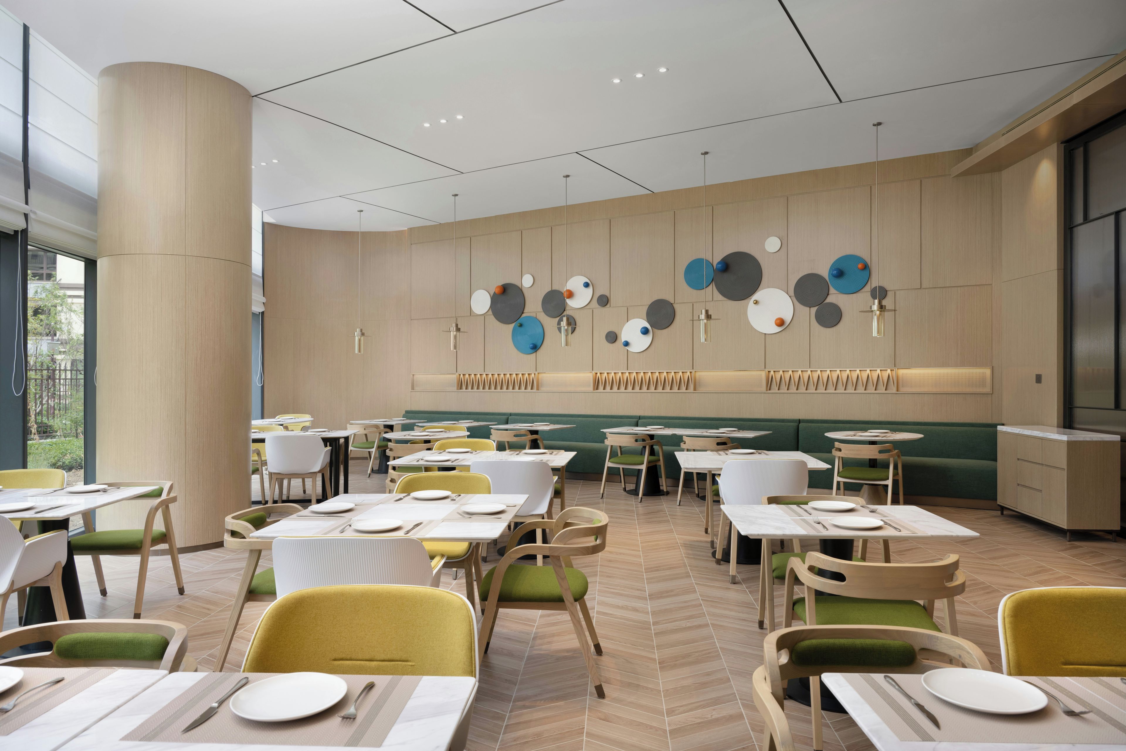 A modern restaurant interior with multiple dining tables, chairs, and a wall with circular decorative elements.