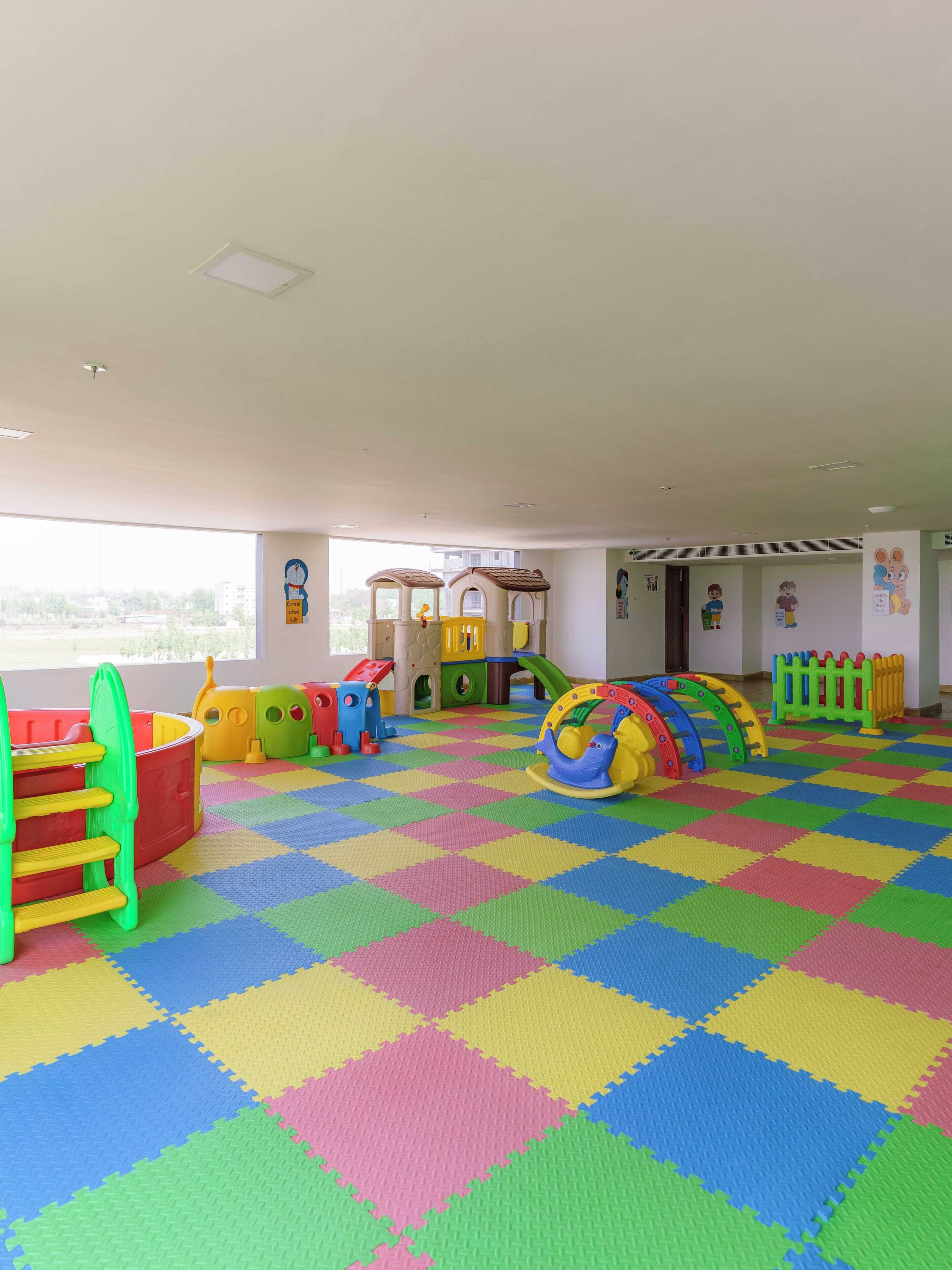 Un salón de juegos con alfombras de espuma de colores, estructuras de juego y vistas al exterior.
