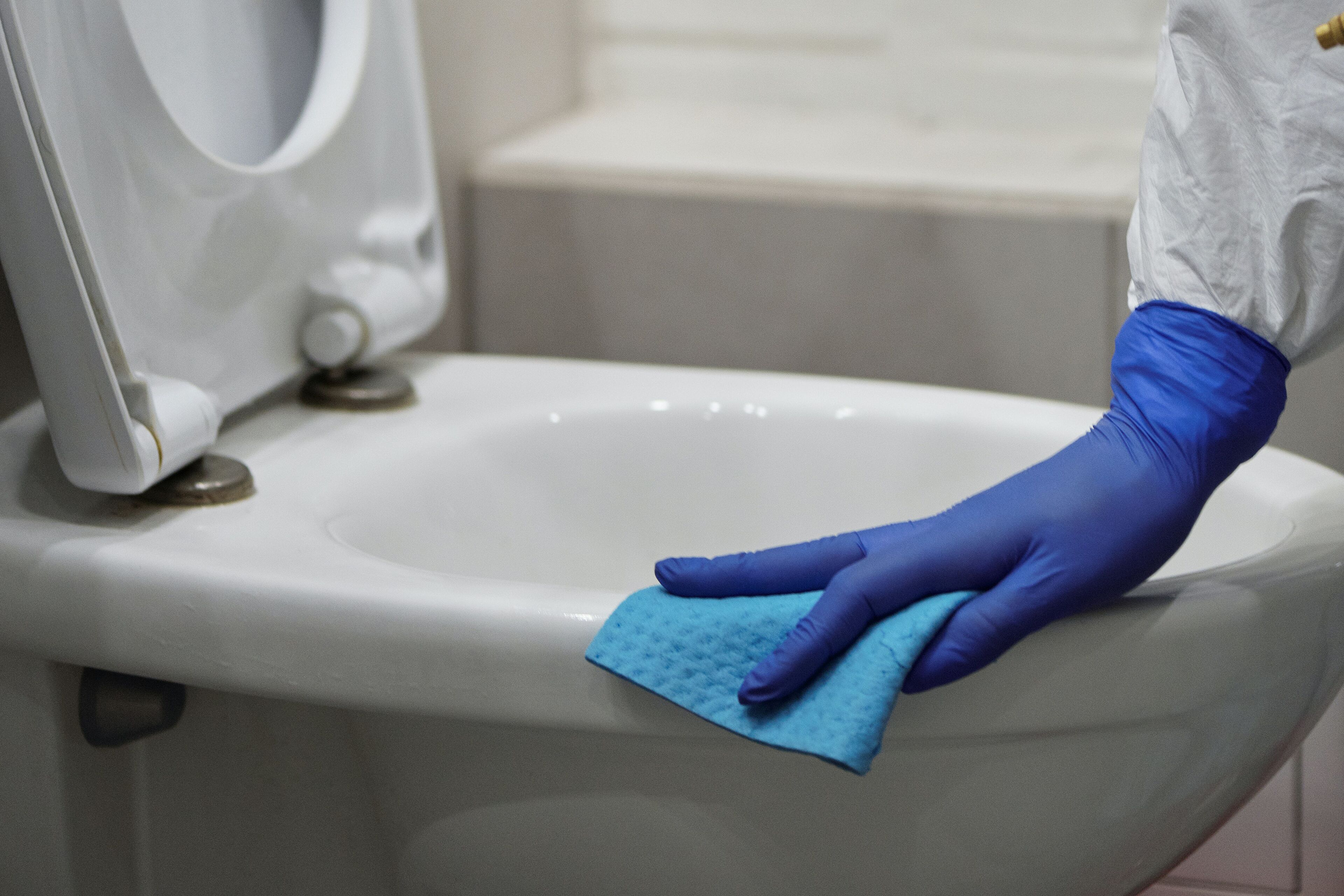 Una persona limpiando un inodoro con un paño azul.