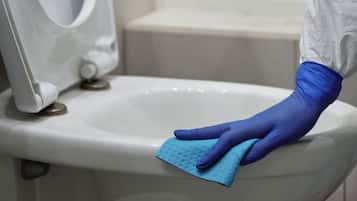 Una persona limpiando un inodoro con un paño azul.