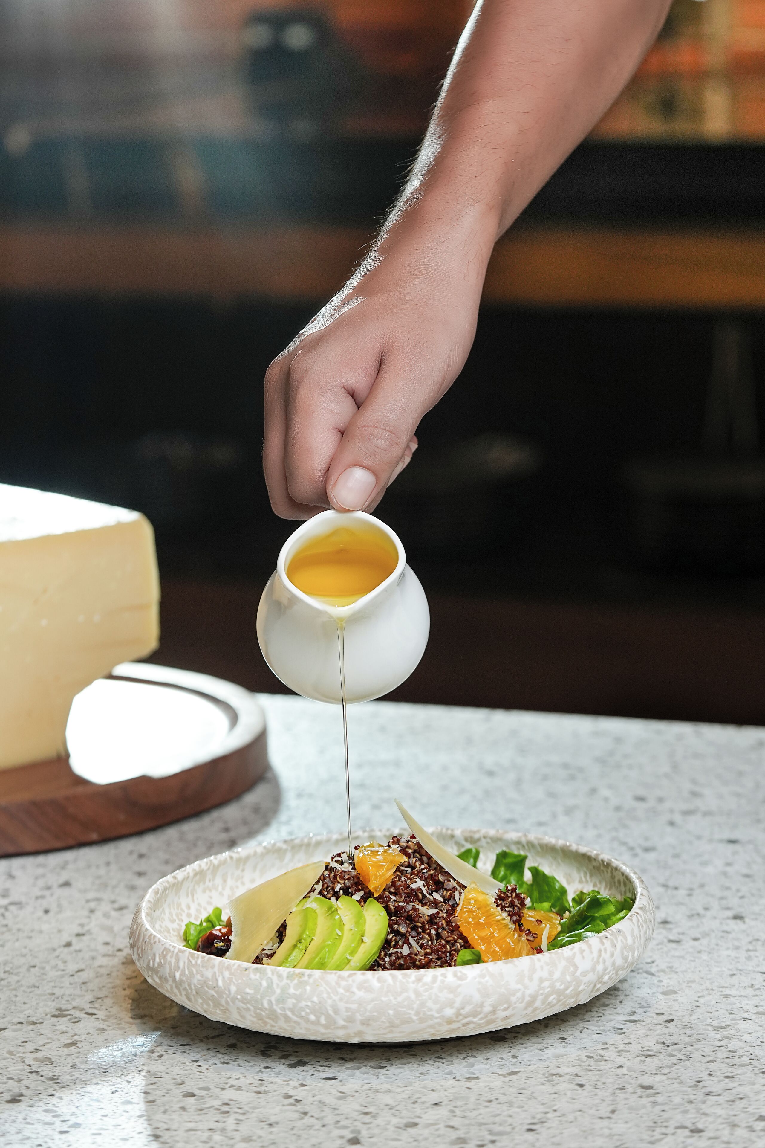 A hand pouring a yellow liquid from a small white jug onto a plate of food.