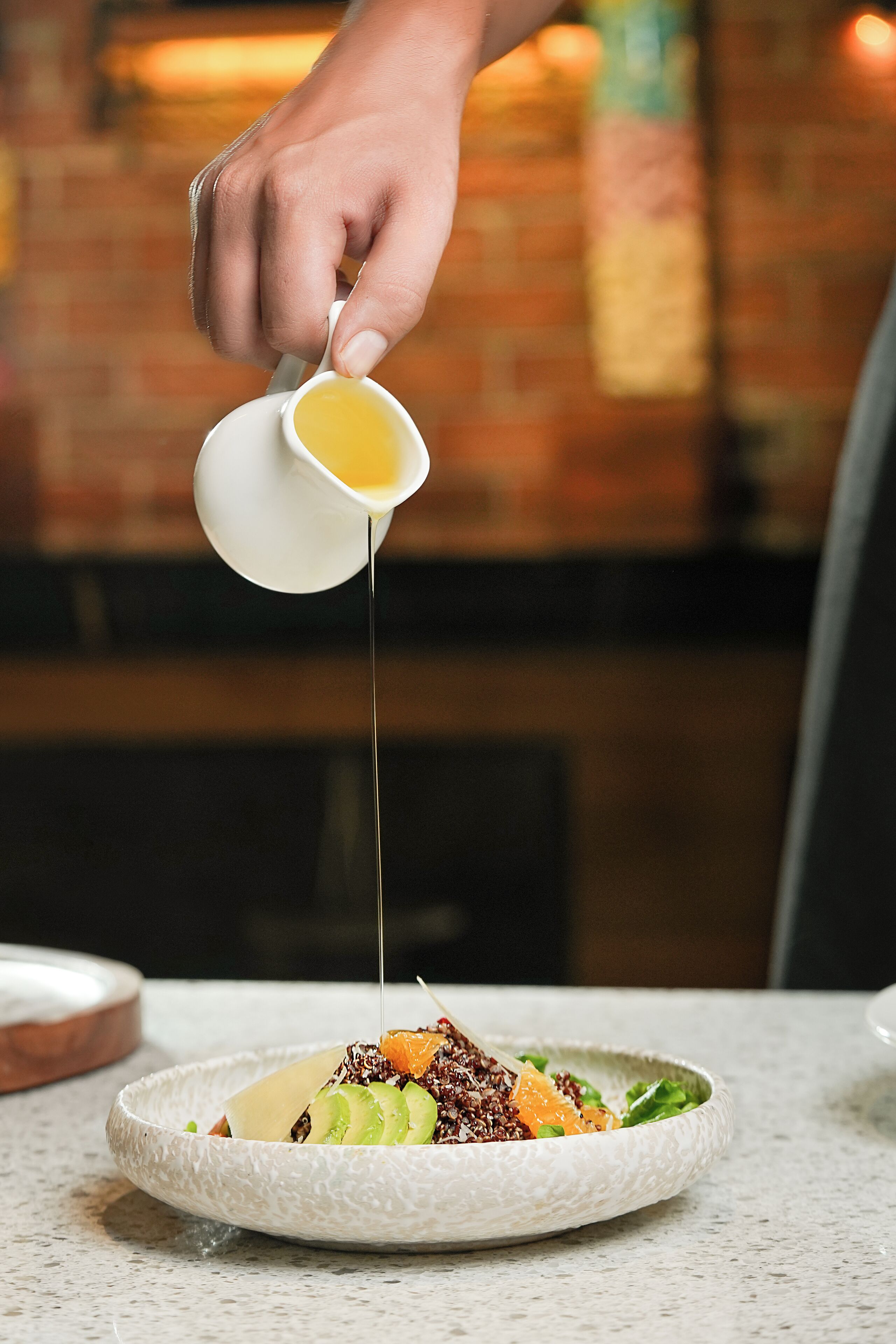 Une main verse de la vinaigrette sur une salade dans une assiette.