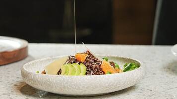 Une main verse de la vinaigrette sur une salade dans une assiette.