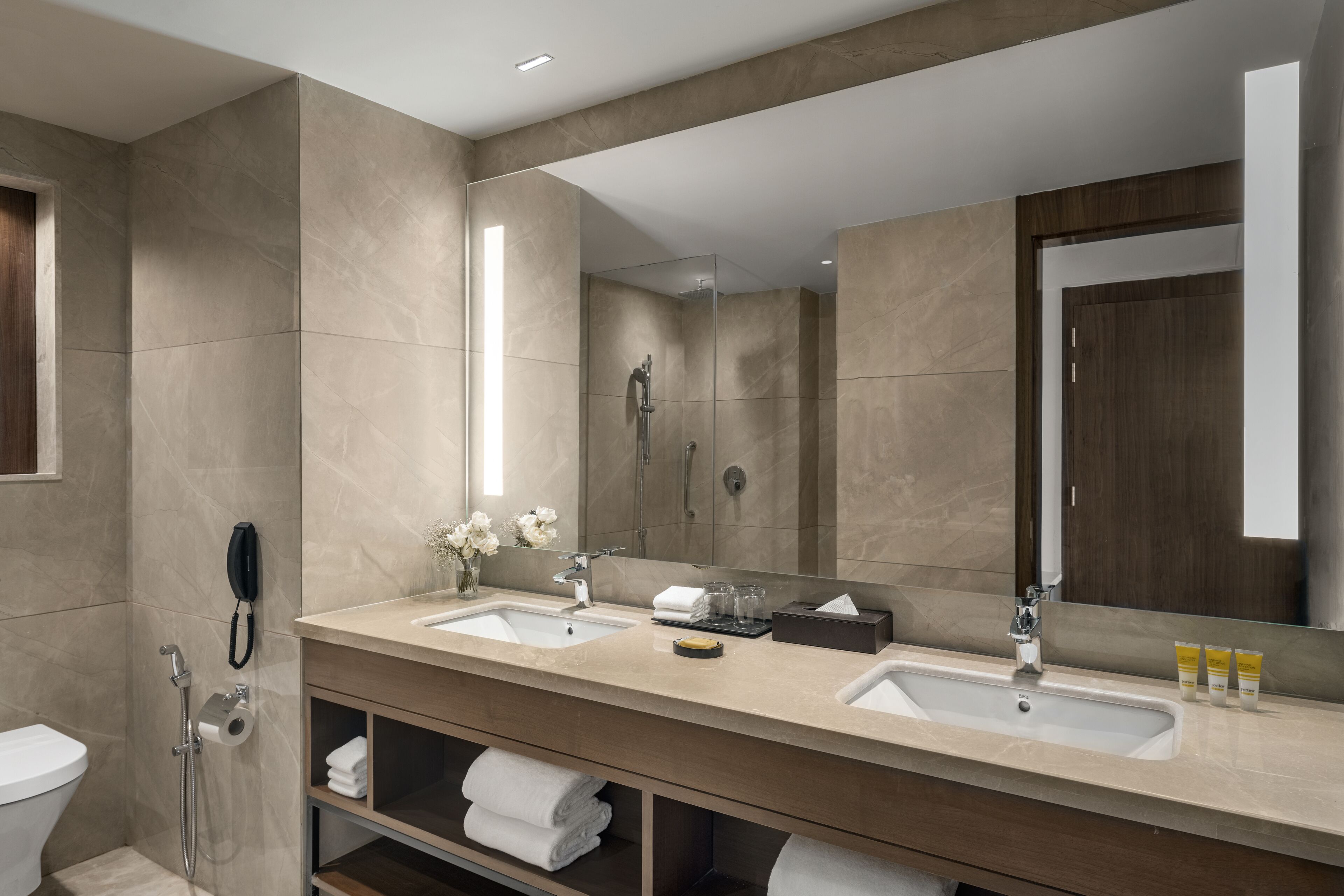 Un baño moderno con dos lavamanos, un espejo grande, una ducha y un inodoro.