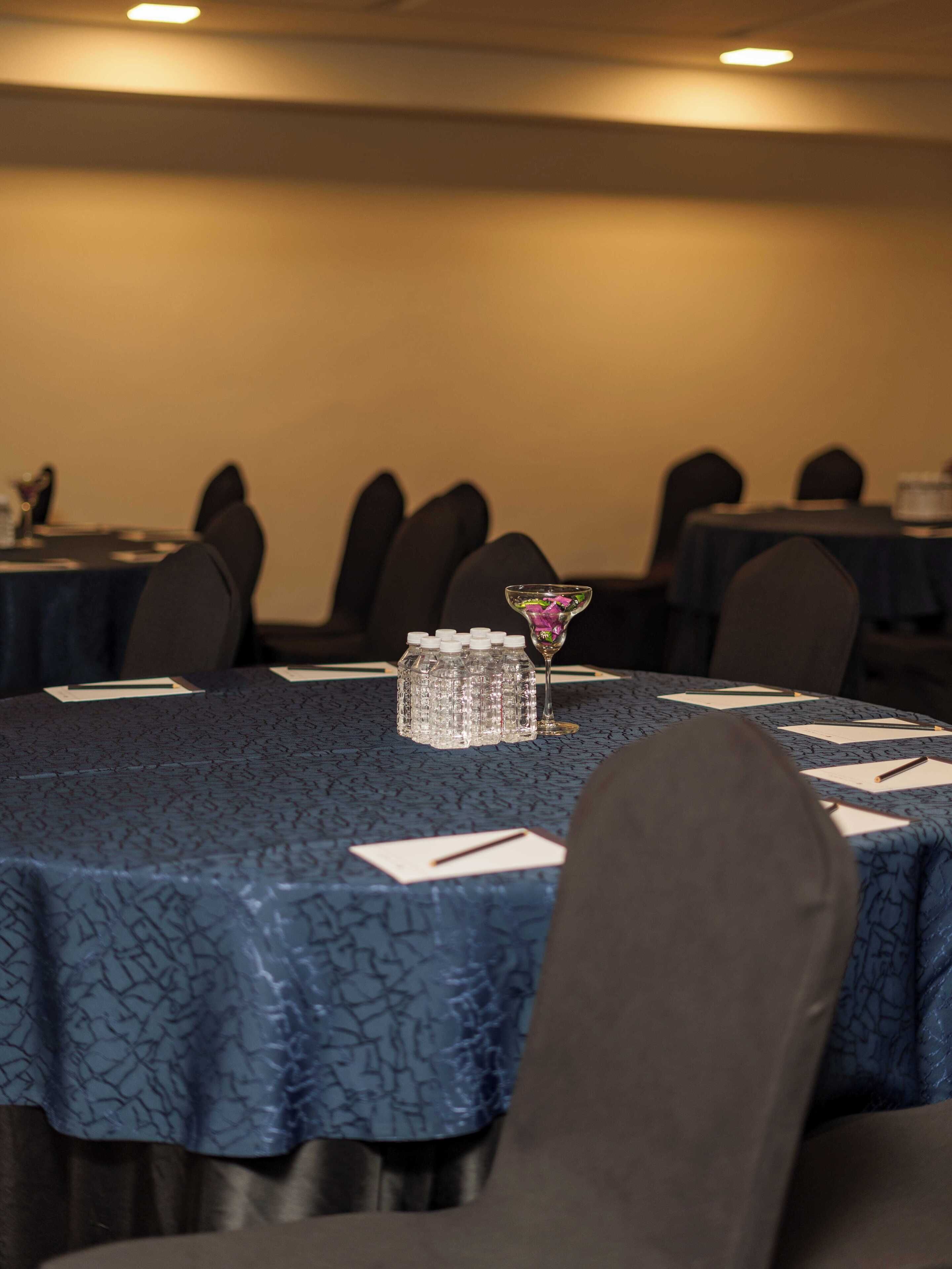 A conference room with tables covered in blue tablecloths, chairs, and a decorative glass vase with a flower.