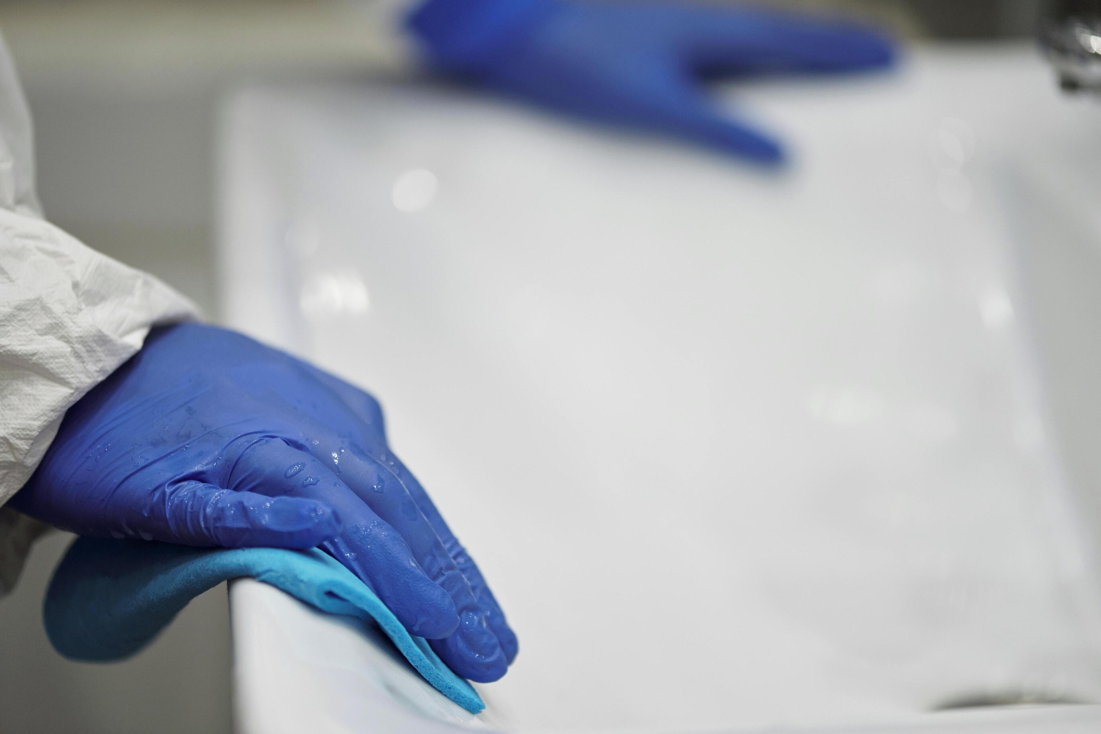 A person wearing blue gloves cleaning a white sink.