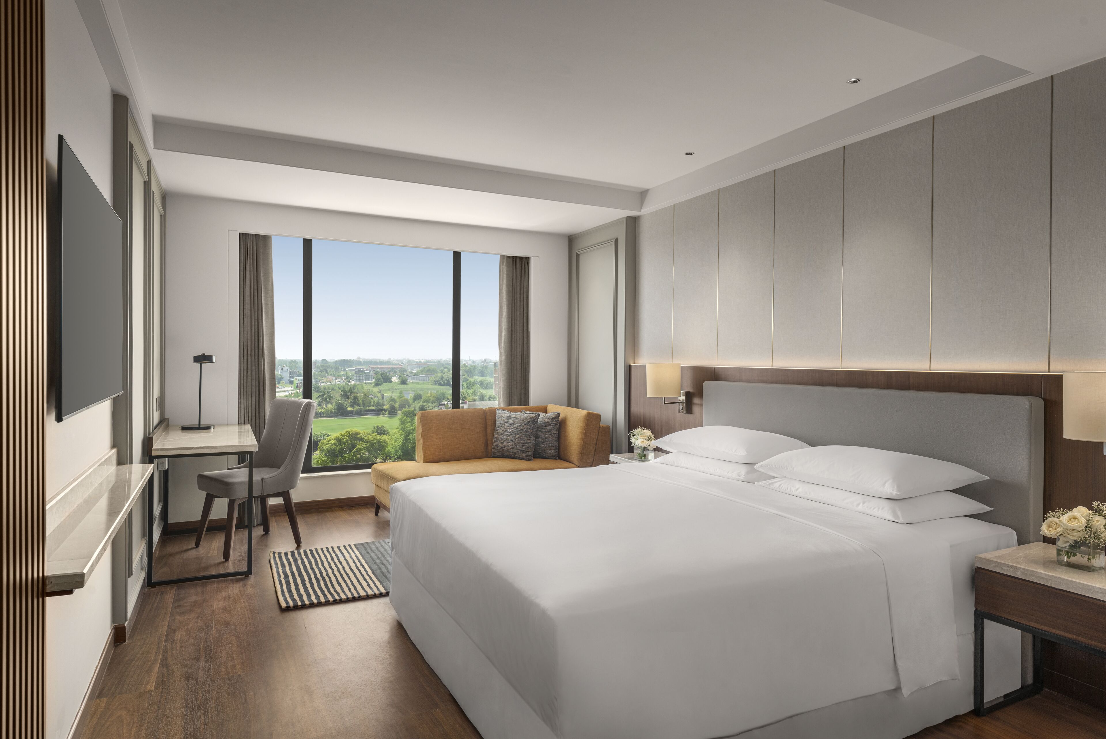 A modern hotel room with a large bed, a desk, and a view of the city.