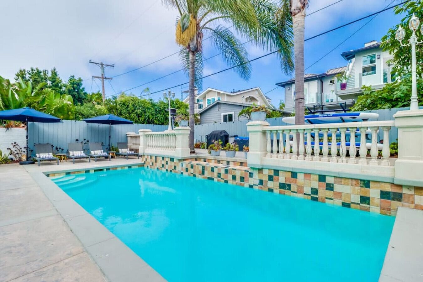 Ein Swimmingpool mit befliesster Kante, umgeben von einem Zaun mit Balustraden, und eine Palme im Hintergrund.