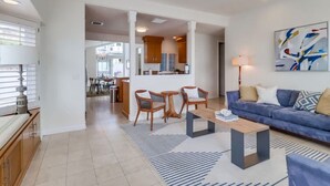 A modern living room with a sofa, coffee table, and chairs. There is a dining area with a table and chairs in the background. - Bayfront Riviera Retreat with Pool and HVAC! (San Diego)