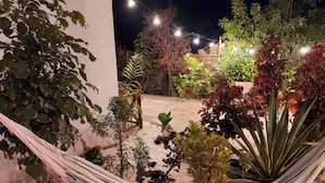 Ein beleuchteter Außenbereich bei Nacht mit einer Hängematte, verschiedenen Pflanzen und Lichterketten.