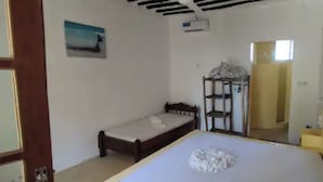 Ein Zimmer mit einem Bett, einem kleinen Tisch, einem Sessel und einem Regal mit Gegenständen.
