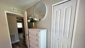 A hallway with a white dresser, a mirror, and a door. - Nearby North Dallas - Grandscapes (The Colony)