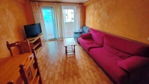 A living room with a wooden floor, a pink sofa, a television, and a small table. - Fantastico Apartamento LA Pineda a 50 Metros de la Playa 2 Habitaciones (Platja de la Pineda)