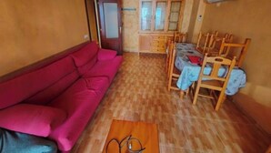 A living room with a red sofa, a dining table with chairs, and a cabinet with glass doors. - Fantastico Apartamento LA Pineda a 50 Metros de la Playa 2 Habitaciones (Platja de la Pineda)