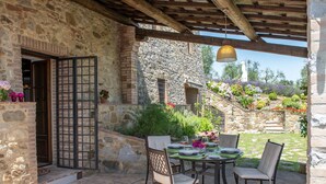 An outdoor patio with stone walls, a wooden pergola, and a table set for dining. - Tuscany Siena Florence Chianti Swimming pool Felsina Brancaia tenuta Arceno. (Toscana)