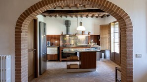 A kitchen with a brick archway, wooden beams, a central island, and a hanging light fixture. - Tuscany Siena Florence Chianti Swimming pool Felsina Brancaia tenuta Arceno. (Toscana)