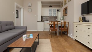 A compact living space with a grey sofa, wooden dining table, and a kitchen area with white cabinets and a TV. - Stylish Apartment in the Center | Balcony and View of the City (Warszawa)