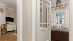A bedroom with a large window, a bed with a brown cover, a dresser, and a television on the wall. - Stylish Apartment in the Center | Balcony and View of the City (Warszawa)