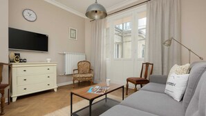 A living room with a sofa, a coffee table, a television, a chair, and a window with curtains. - Stylish Apartment in the Center | Balcony and View of the City (Warszawa)