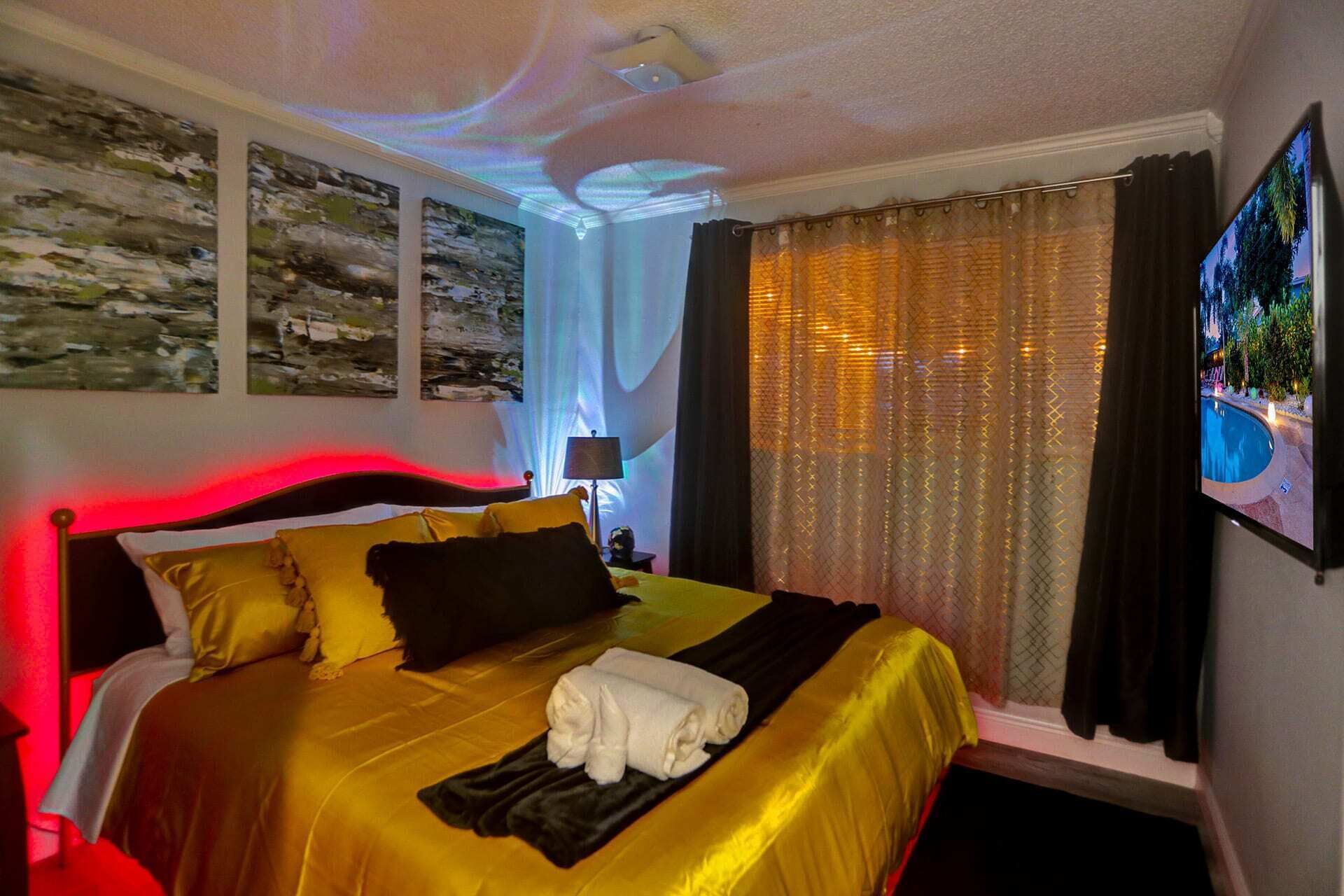 A hotel room with a large bed, a flat-screen TV, and artwork on the walls.