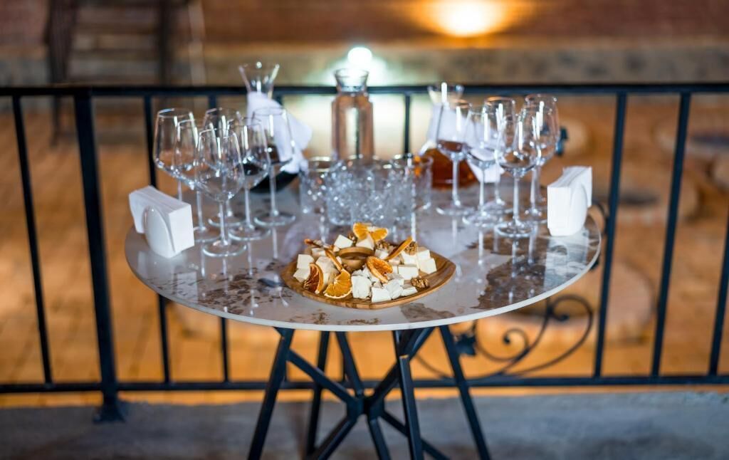 Een ronde tafel met een wit kleed, omringd door lege wijnglazen en een decoratief etenstje in het midden.