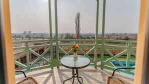 Ein Balkon mit Tisch und Stühlen, einer Blumenvase und Blick auf eine Landschaft mit Bäumen und einem Gebäude im Hintergrund.
