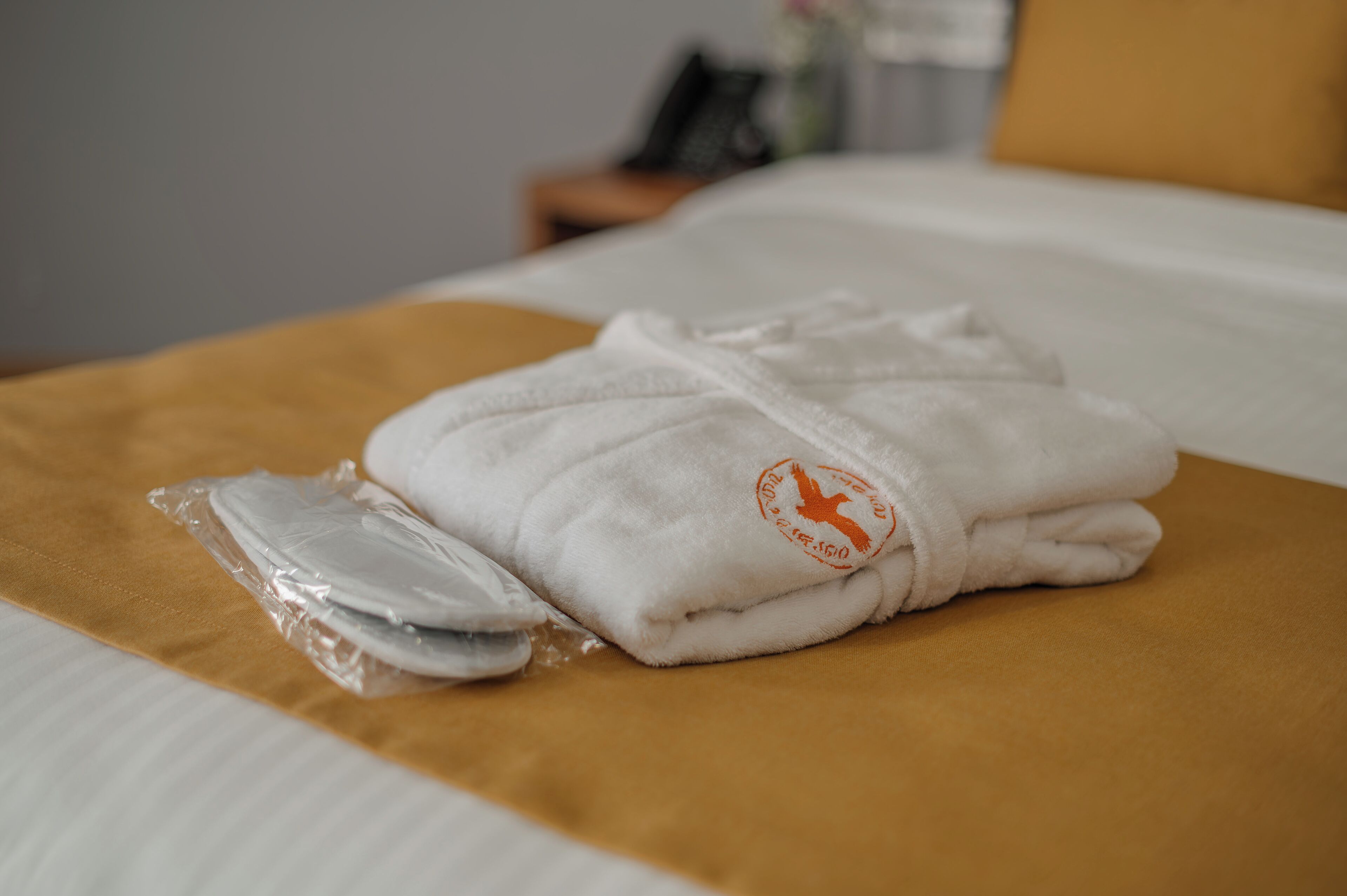 Una cama bien hecha con una toalla blanca y un paquete de plástico sobre un edredón amarillo.