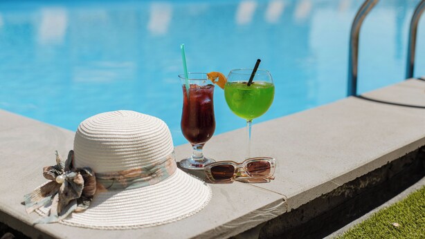 Ein Poolbereich mit Hut, Sonnenbrille und zwei Getränken auf einem Betonrand.